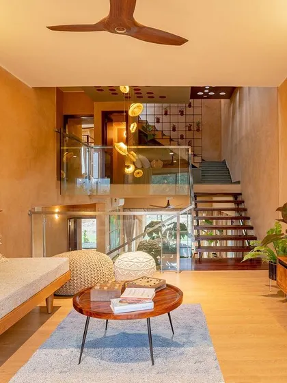 The informal living area on the upper floor is a cozy retreat. A comfortable daybed, woven poufs, and a simple wooden media console create a relaxed atmosphere. The space overlooks the central atrium, maintaining a sense of connection to the rest of the home.