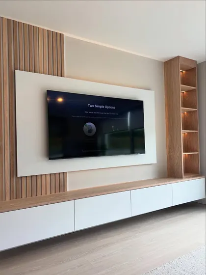 An angled view of a modern entertainment center, showing how the different elements like the wooden paneling, white TV mount, and open shelving come together to create a balanced and functional design.