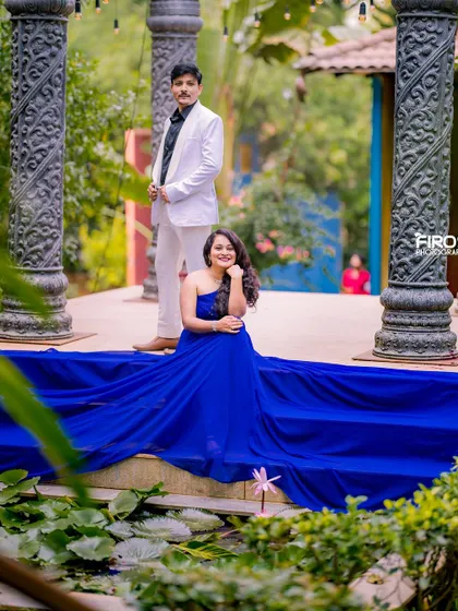A stylish couple portrait at the stone structure. The bride's flowing blue gown drapes over the steps, while her partner stands behind her in a crisp white suit.
