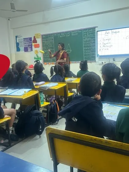 A classroom at Cambridge School where a teacher is using real-world objects (bananas) to teach shapes. This connects abstract concepts to the children's everyday lives.