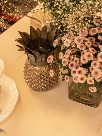 A close-up of a brass pineapple container next to a simple arrangement of pink chrysanthemums. I enjoy mixing classic motifs with fresh flowers to create table decor that is both elegant and inviting.