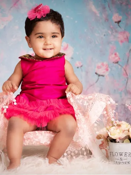 Dressed in a vibrant pink dress against a beautiful floral backdrop, this little girl's smile lights up the entire photo. These sessions are all about capturing the pure joy of being a baby.