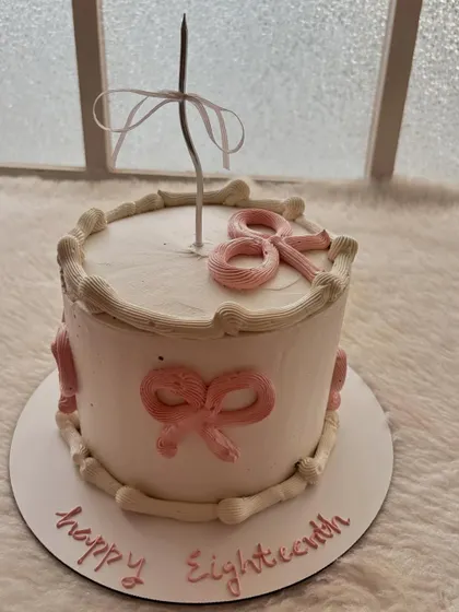 A simple and sweet cake for an 18th birthday, decorated with delicate pink bows and a single candle.