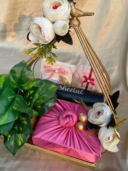 A heartfelt goodbye hamper for a senior. This gift features a Furoshiki-wrapped present, a personalized jewelry organizer, and white flowers, all arranged in a golden metal basket.