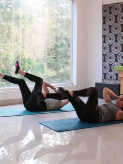 Two students practicing the Pilates Obliques exercise in sync. Group classes are a great way to build energy and motivation.
