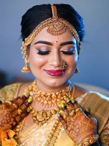 A stunning portrait of the bride Lavanya, her face glowing and her hands, adorned with a rich mehendi stain, framing her jewelry.