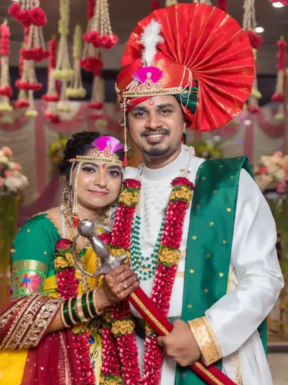 A regal portrait of the bride and groom in their traditional Maharashtrian wedding attire, holding a ceremonial sword.