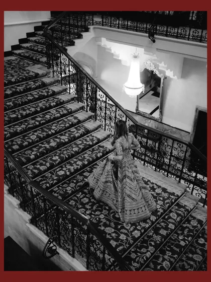 A dramatic black and white shot of the bride descending the iconic staircase of the Taj Mahal Palace. The high angle and architectural details create a grand and timeless image.