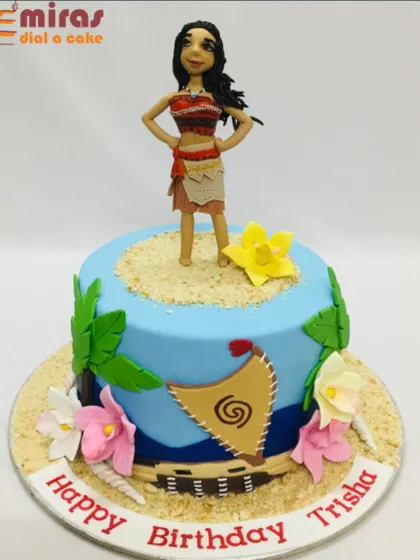A beautiful Moana cake featuring a hand-sculpted figurine of the adventurous princess. The cake is decorated with an ocean theme, tropical flowers, and sandy textures.