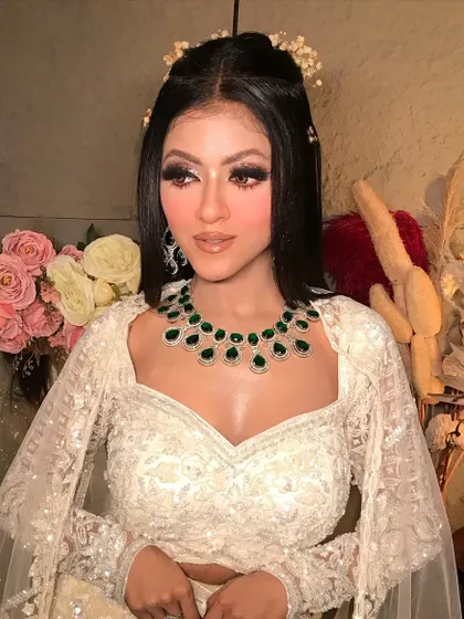 A close-up of the glam evening look. The focus is on the dramatic winged eyeliner, flawless skin, and the stunning contrast of the emerald green jewelry.