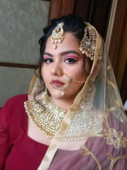 The model is draped in a delicate net dupatta, showing how the makeup and heavy jewelry work together under traditional veiling.
