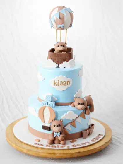 This two-tier teddy bear cake is perfect for a first birthday or baby shower, with adorable bears, a hot air balloon, and a soft blue and brown color palette.