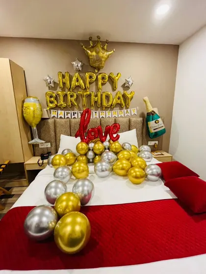 A royal-themed birthday room decoration. This setup includes 'Happy Birthday' foil letters with a crown, champagne balloons, and gold and silver balloons on the bed.