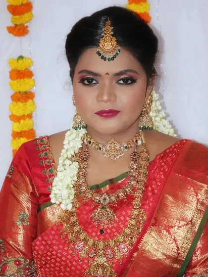 A powerful and traditional look for a muhurtham. The makeup is bold and defined, with strong eyes and lips that match the richness of the red silk saree and heavy gold jewelry.