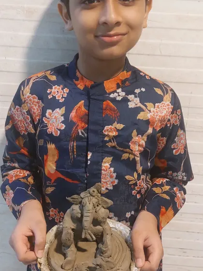 A young boy proudly holds his handcrafted Ganesha idol. Our workshops are designed to build confidence and give children a sense of ownership over their festive creations.