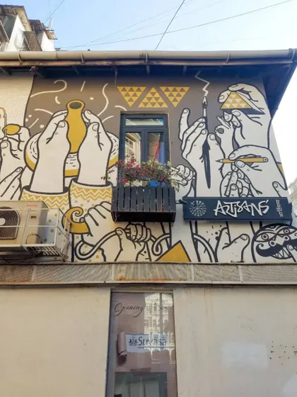 The exterior of the Artisans' gallery in Kala Ghoda, featuring a mural of many hands engaged in creative acts like painting and sculpting. The art perfectly reflects the purpose of the building.