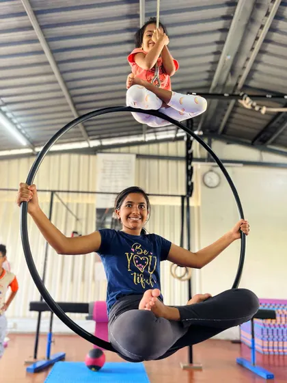 A super sister duo. One sister provides a strong foundation on the aerial hoop while the other balances above, showcasing their bond and teamwork.
