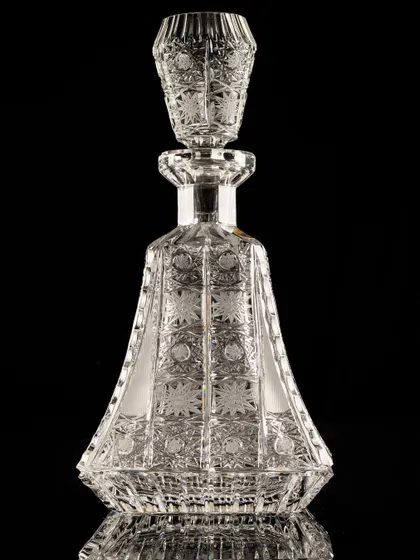 A beautifully intricate crystal decanter shot on a black background. The lighting is designed to catch every facet, showcasing the high level of craftsmanship.