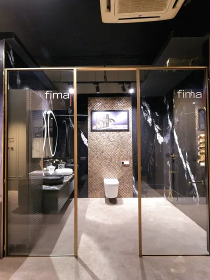 An elegant glass doorway with a gold frame provides a grand entrance to this luxurious bathroom display in the Fima showroom.