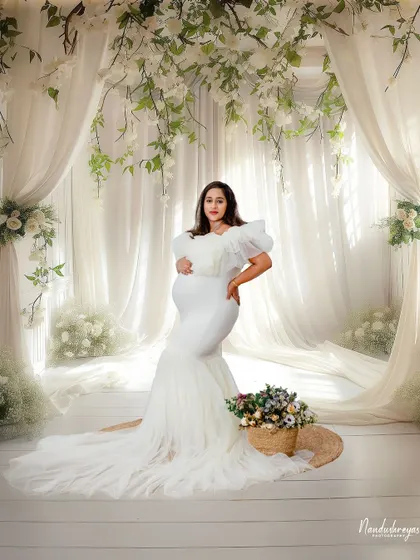 A breathtaking shot of the mother-to-be in a white gown, surrounded by curtains of hanging white flowers. This is my signature "angelic" studio setup.