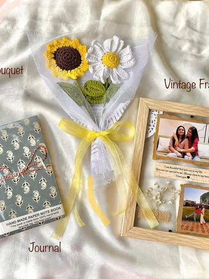 A beautiful and rustic-themed gift set. This hamper combines a vintage-style transparent photo frame, a handmade journal, and a sunflower and daisy crochet bouquet.