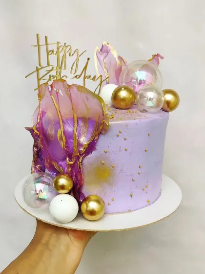 A glamorous purple cake with gold dust, gold and iridescent spheres, and purple rice paper sails. A true statement piece for a birthday.
