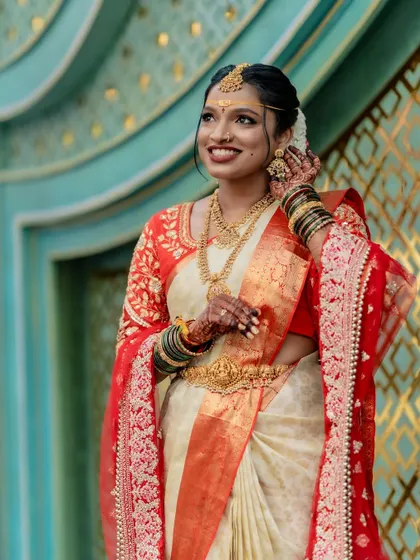 A three-quarter view of the bride, highlighting the neat shoulder pleats and the way the pallu is draped over the arm. The addition of a sheer red dupatta adds another layer of elegance to the ensemble.