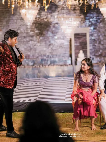 Fun and games at the sangeet, with the host engaging the couple and guests under the glamorous disco ball and chandelier setup.