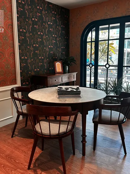 Another corner of my showroom, featuring a marble-topped dining table and wooden chairs set against a backdrop of contrasting wallpapers, showcasing my eclectic style.