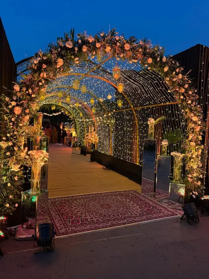 A stunning entrance tunnel for a sangeet night, created with arches wrapped in fairy lights and adorned with flowers. The glowing pathway leads guests into a night of celebration and dance.