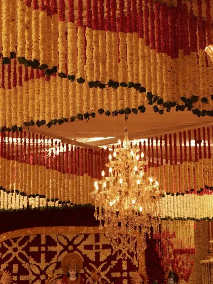 A view looking up at the intricate floral ceiling, where rows of red and yellow garlands create a vibrant pattern. A crystal chandelier hangs in the center, its light sparkling against the petals.