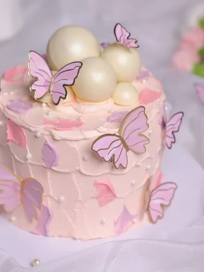 We create a magical garden with this pink butterfly cake. A flurry of pink and gold butterflies appears to dance around the cake, which is decorated with abstract pink frosting and shimmering white chocolate spheres, perfect for a whimsical birthday.