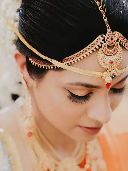 A detailed shot of a South Indian bride's 'maang tikka' and flawless makeup. We pay close attention to the intricate jewelry and bridal details.