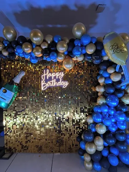 The gold shimmer wall and balloon arch create a perfect, glamorous photo booth for a birthday party.