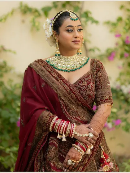 A classic three-quarter portrait of the bride, showcasing her complete bridal look, from her jewelry and makeup to her richly embroidered lehenga.