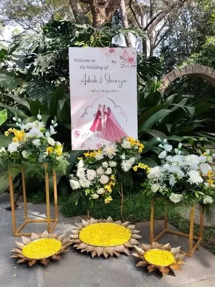 A personalized welcome sign for a Haldi event, surrounded by floral arrangements in shades of yellow and white, setting a sunny and happy tone right from the entrance.
