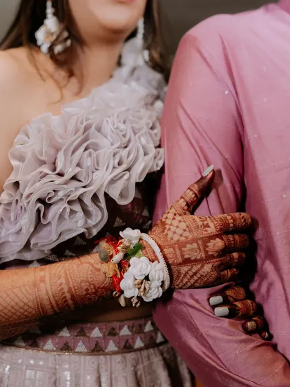 A close-up shot of the bride's hands, adorned with intricate mehendi and floral bracelets, holding the groom's arm.