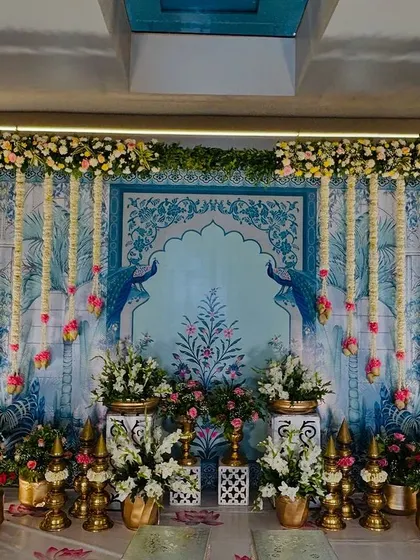A beautiful stage with a Pichwai painting backdrop, framed by floral arrangements and hanging jasmine garlands.
