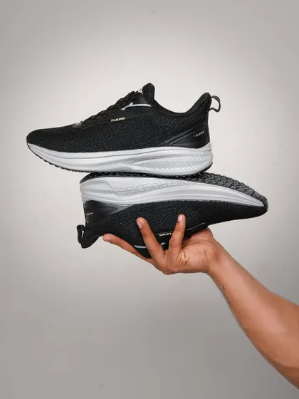 A hand-held shot showcasing a pair of black running shoes. This pose gives a clear view of the shoe's profile and sole, highlighting its design and structure in a simple, clean way.