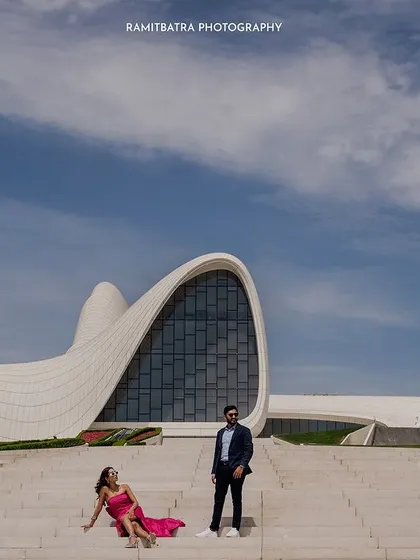 A wide shot of the couple on the steps of the Heydar Aliyev Centre, with the unique building and a vast blue sky.