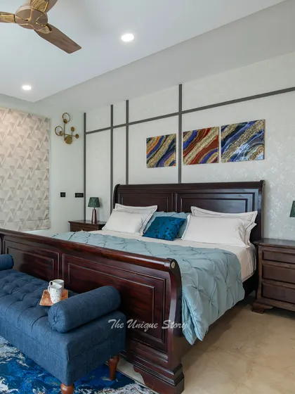 A full view of the luxurious bedroom, featuring a stately wooden sleigh bed, a plush blue bench, and a feature wall with geometric paneling. The abstract artwork and patterned rug add layers of interest to the space.