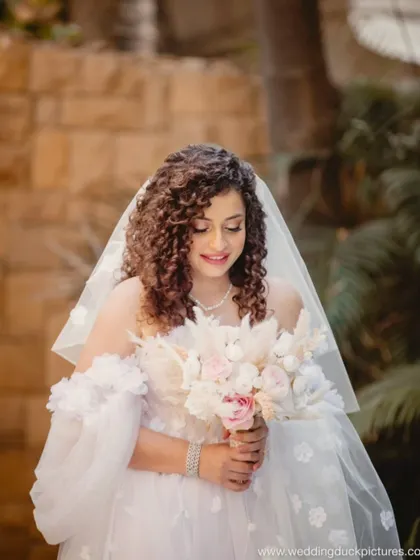 A serene portrait of the curly-haired bride. Her soft makeup and beautiful bouquet create a look of gentle, romantic elegance.
