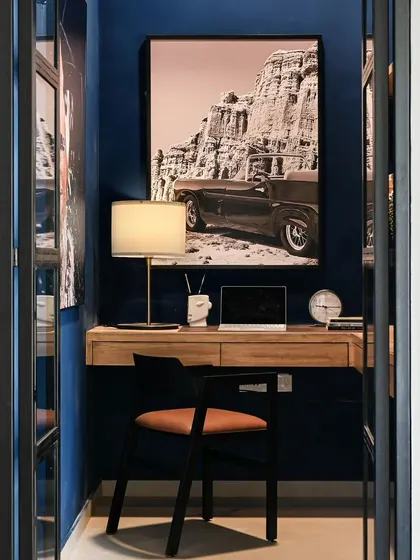 This moody blue home office was carved out of a small, doorless space. I added see-through glass and metal doors for privacy without making the room feel smaller. The L-shaped desk and oversized art create a cool, functional backdrop for video calls.