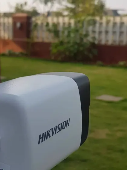 A Hikvision 4MP IP bullet camera installed and focused on the garden and perimeter fence of a property.