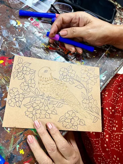 A participant carefully carving a detailed bird and flower design into a woodblock for printing.