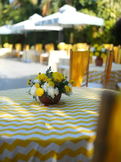 Guest seating at a Haldi function with cheerful yellow and white chevron-patterned tablecloths.