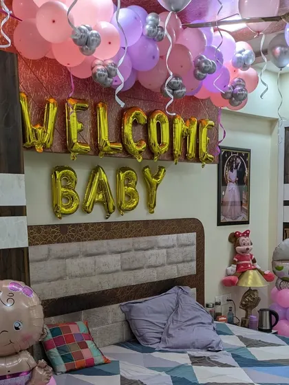 A bedroom decorated to 'Welcome Baby', with gold foil letters above the bed and a ceiling covered in pink, purple, and silver balloons.