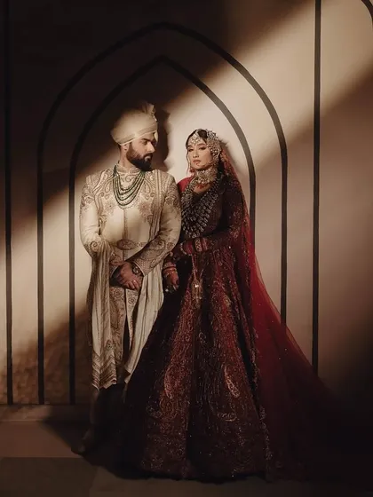 Styling a couple for a coordinated royal look. The bride's deep maroon lehenga complements the groom's ivory sherwani, creating a timeless and cinematic portrait of togetherness.