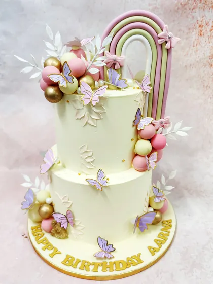 We craft an ethereal dream with this two-tiered rainbow butterfly cake. A soft pastel rainbow arch, delicate butterflies, and clusters of pink, gold, and cream spheres come together to create a whimsical and sophisticated masterpiece.