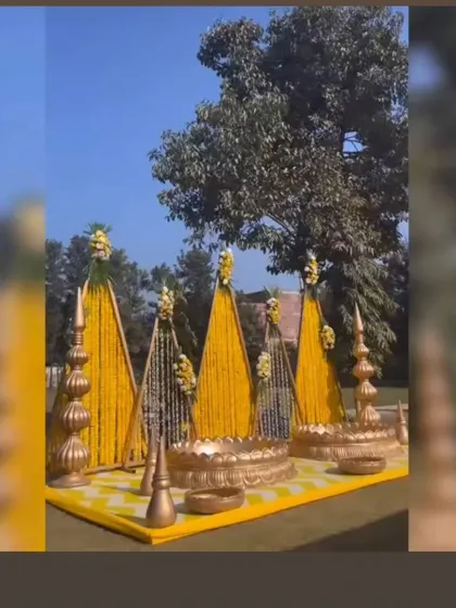 A grand outdoor Haldi setup with large triangular structures covered in marigold strings. The golden urlis and props add a royal touch to the entire decor.